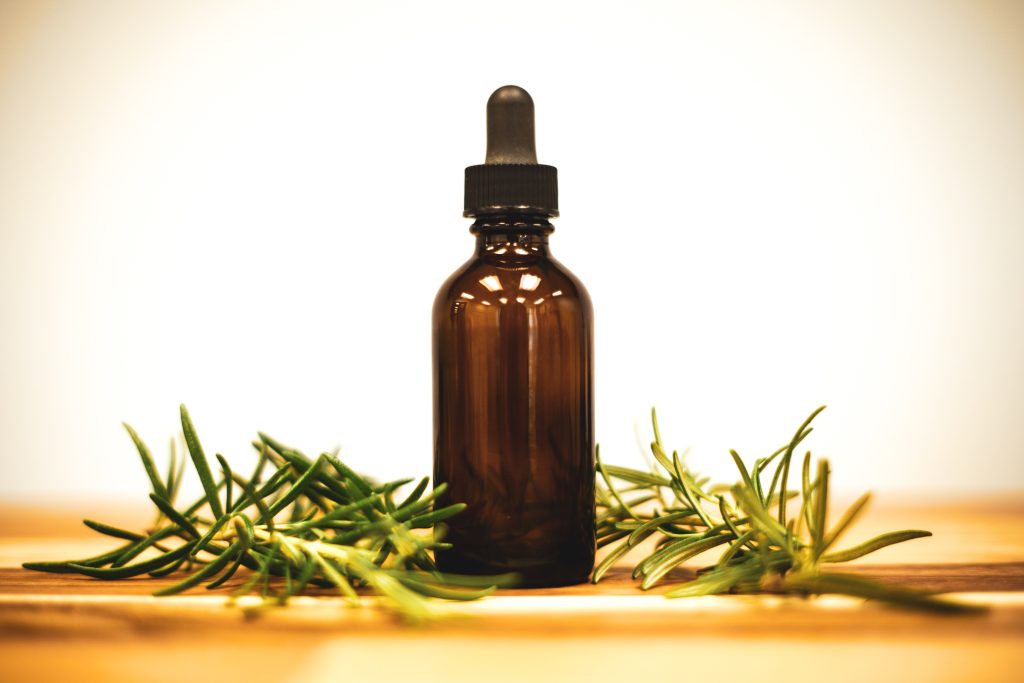 Flacon d'huile essentielle posé à côté d'herbes aromatiques, base d'un répulsif anti-moustique naturel