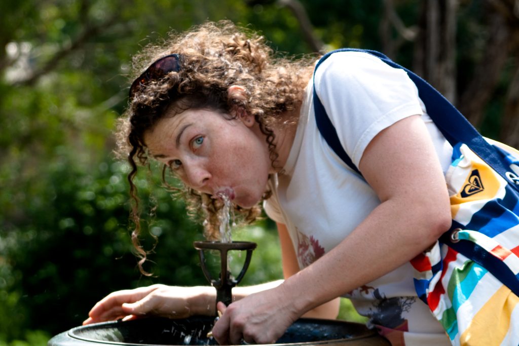 Femme s'hydratant a une fontaine d'eau, illustrant l'importance de boire suffisamment en ete