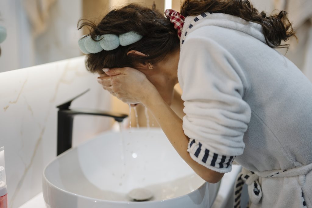 Femme se nettoyant le visage à l'eau au-dessus d'un lavabo