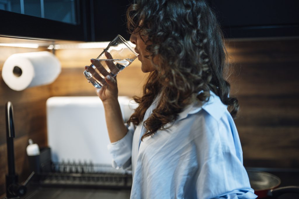 Maman qui allaite buvant un grand verre d’eau pour rester hydratée en été
